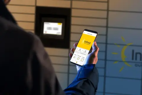 Osoba korzysta z aplikacji InPost na telefonie, by nadać paczkę. W tle widać Paczkomat.