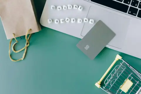 Karty płatnicze, torba i mini wózek na zakupy na laptopie symbolizują wygodne **alsendo** zakupy online.