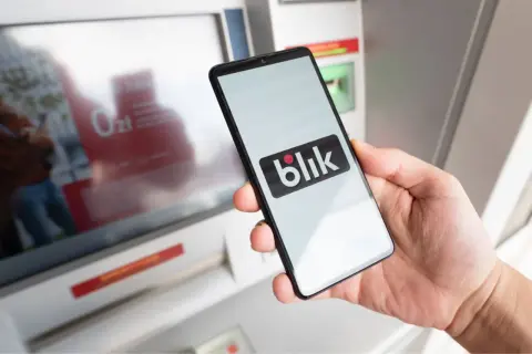 Dłoń trzyma smartfon z logo Blik przed paczkomatem. Czy w paczkomacie można płacić kartą? Blik to alternatywa.