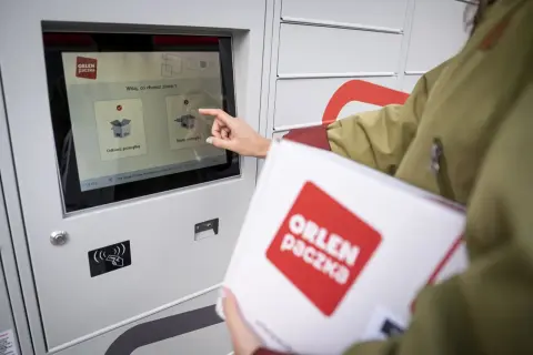 Kobieta dotyka ekranu automatu, by nadać paczkę Orlen. Wybiera opcję "Nadaj przesyłkę".