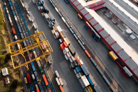 Widok z lotu ptaka na terminal kolejowy, gdzie odbywa się transport intermodalny. Żurawie przeładowują kontenery między pociągami a ciężarówkami.