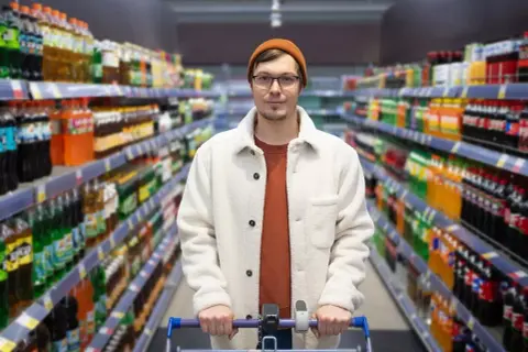 Mężczyzna z wózkiem sklepowym w alejkach pełnych napojów. Branża retail w praktyce, gdzie wybór jest ogromny.