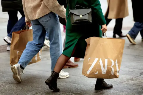Ludzie idący ulicą z torbami na zakupy. Jedna z toreb ma wyraźne logo ZARA, sugerując udany zwrot lub zakupy w tym sklepie.