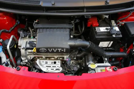 Silnik VVT-i w czerwonym Yaris 2. Widoczny akumulator, elementy układu dolotowego i chłodzenia.