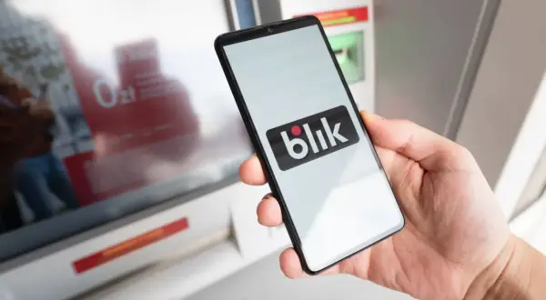 Dłoń trzyma smartfon z logo Blik przed paczkomatem. Czy w paczkomacie można płacić kartą? Blik to alternatywa.