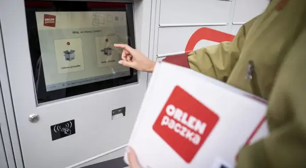 Kobieta dotyka ekranu automatu, by nadać paczkę Orlen. Wybiera opcję "Nadaj przesyłkę".